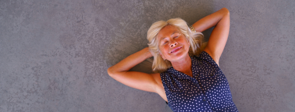 Happy senior woman lying at a concrete floor, wide photography. Copy space.