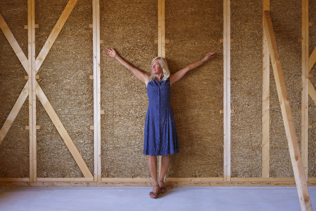 A happy senior woman inside of her new unfinished ecological wooden house.