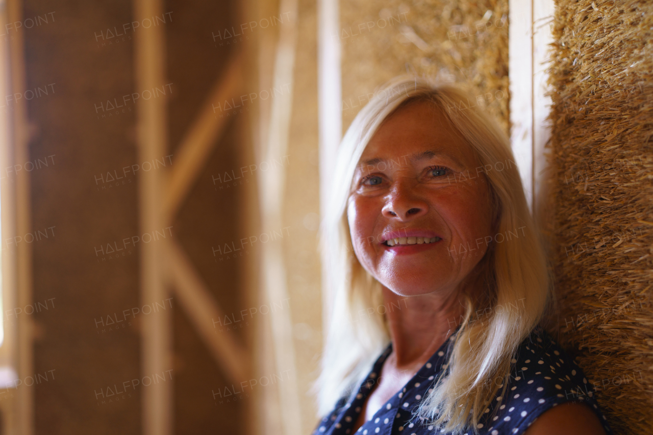 Portrait of happy senior woman inside of her unfinished ecological wooden house.