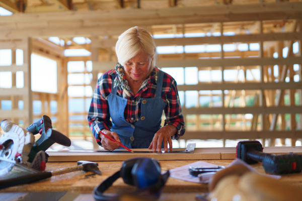 Senior woman working inside of her unfinished ecological sustainable wooden eco house. Concept of active independent women and seniors, eco house and healthy lifestyle.