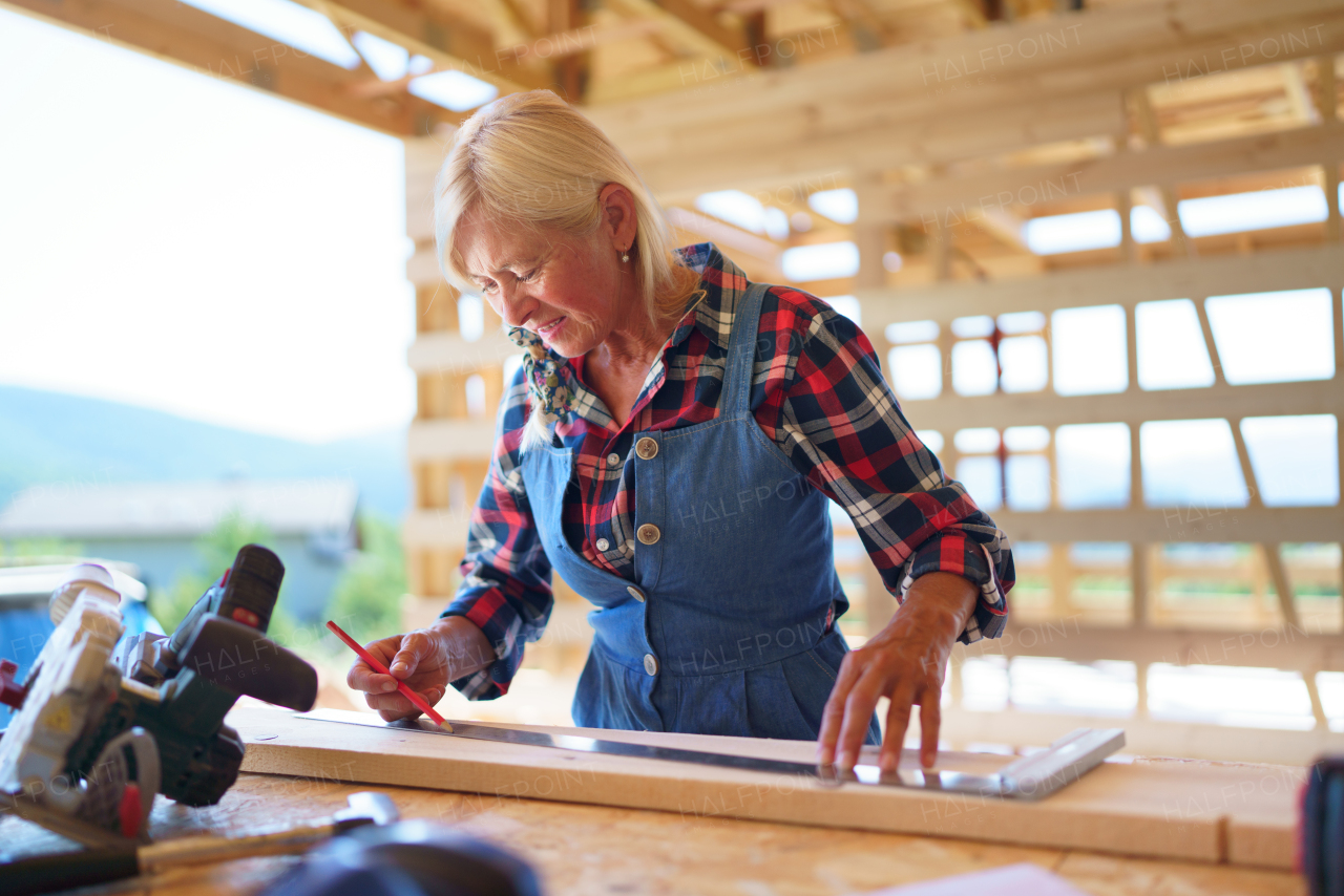 Senior woman working inside of her unfinished ecological renewable low energy sustainable wooden eco house. Concept of active independent women and seniors, eco house and healthy lifestyle.