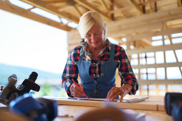 Senior woman working inside of her unfinished ecological sustainable wooden eco house. Concept of active independent women and seniors, eco house and healthy lifestyle.