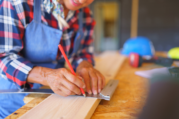 Close up of a senior woman measuring wooden board inside of her unfinished ecological wooden eco house.