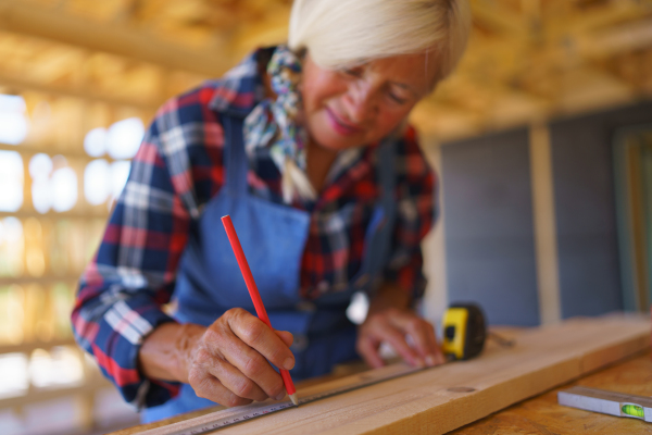 A senior woman measuring wooden board inside of her unfinished ecological wooden eco house.