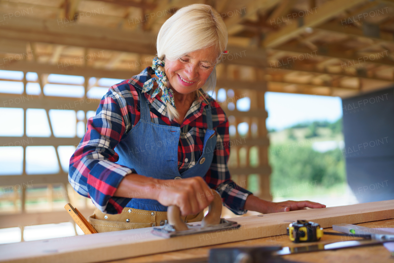 Senior woman working inside of her unfinished ecological renewable low energy sustainable wooden eco house. Concept of active independent women and seniors, eco house and healthy lifestyle.