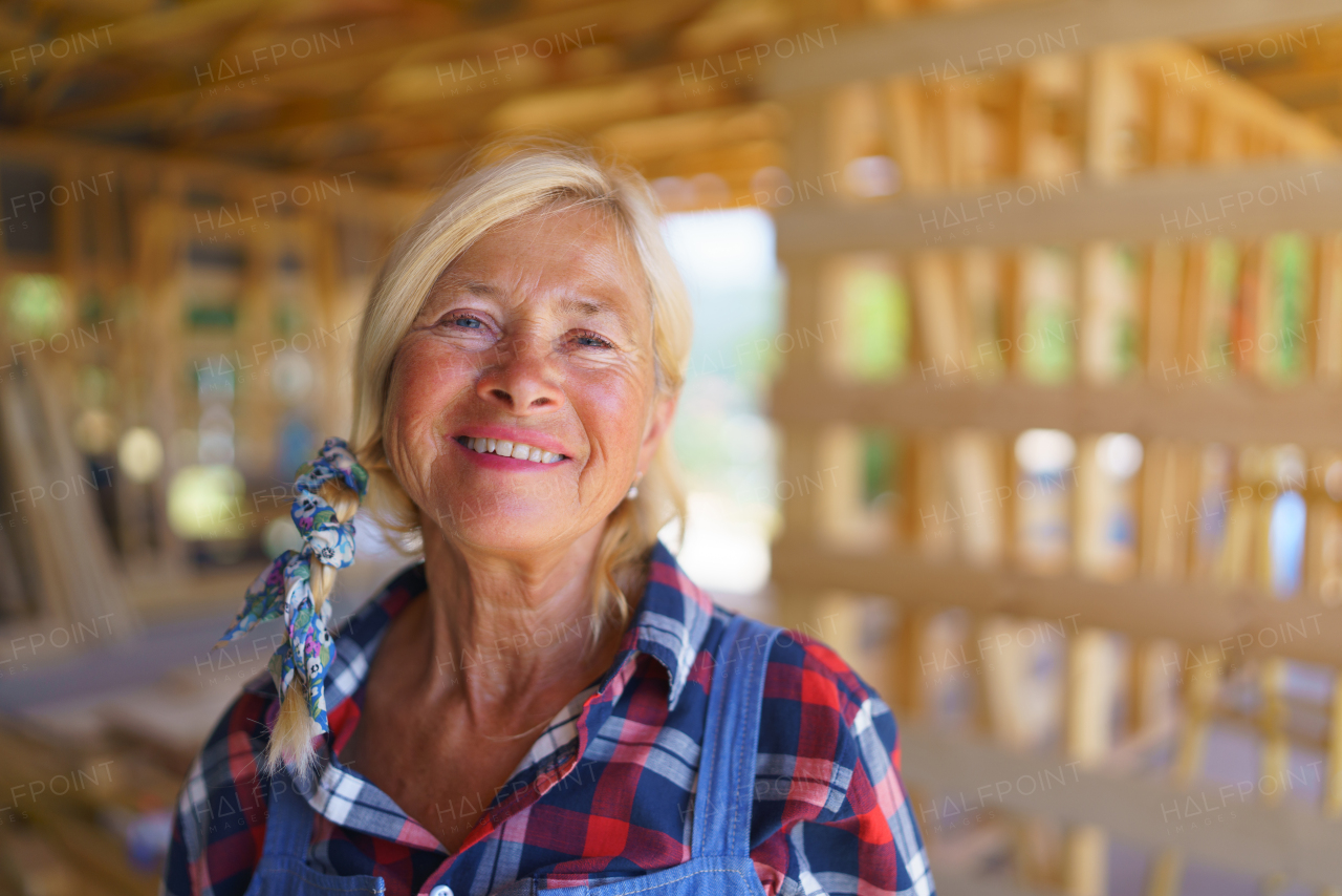 Portrait of happy senior woman working inside of her unfinished ecological sustainable wooden eco house. Concept of active independent women and seniors, eco house and healthy lifestyle.