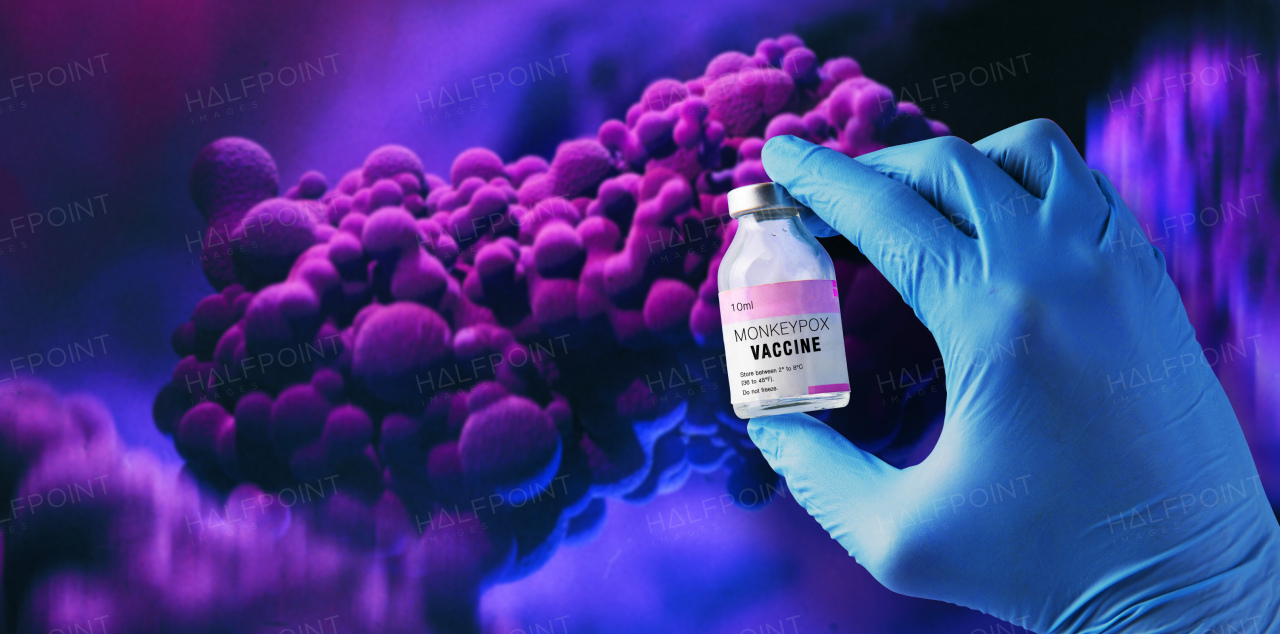 A doctor's hand holding monkeypox vaccine with microscopic view of floating monkeypox virus cells or molecules in background.