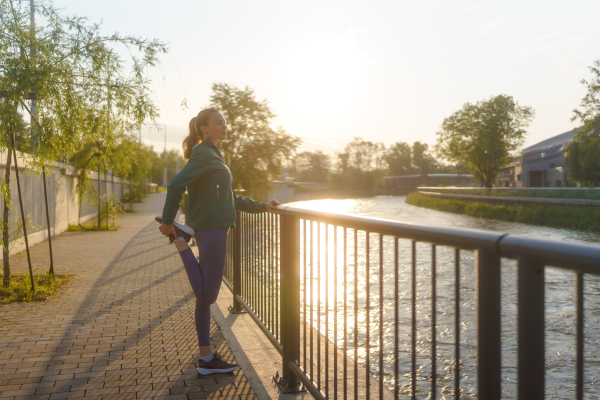 Young female runner stretching before her early morning run. Fitness girl in sportswear preparing for evening exercise. Outdoor workout concept.