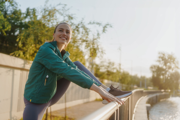 Young female runner stretching legs before her early morning run. Waist up portrait of fitness girl in sportswear preparing for evening exercise. Outdoor workout concept.