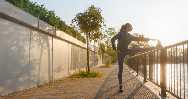 Athletic young woman in sportswear doing streching exercises before morning run. Fitness girl preparing for evening exercise. Outdoor workout concept.