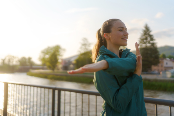 Young female runner stretching before her early morning run. Fitness girl in sportswear preparing for evening exercise. Outdoor workout concept.