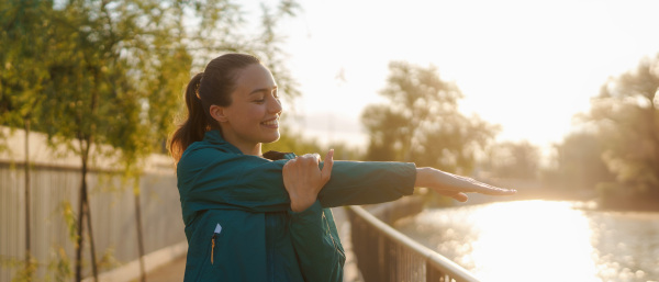 Young female runner stretching arms before her early morning run. Waist up portrait of fitness girl in sportswear preparing for evening exercise. Outdoor workout concept.