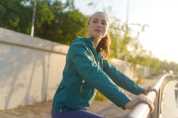 Young female runner enjoying sunrise before her early morning run. Waist up portrait of fitness girl in sportswear preparing for evening exercise. Outdoor workout concept.