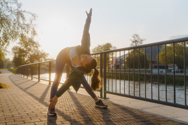 Young female runner stretching before her early morning run. Fitness girl in sportswear preparing for evening exercise. Outdoor workout concept.