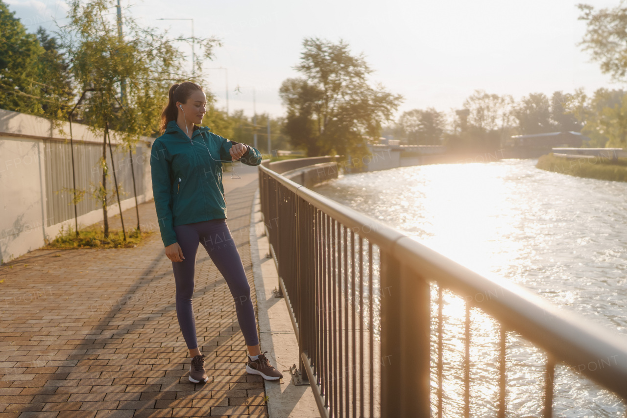 Young woman runner checking her performance on smartwach after workout session. Athletic girl preparing for a morning jogging. Outdoor Workout concept.