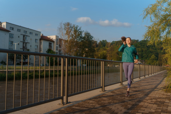 Young woman runner listening music with headphones. Athletic girl listening music while jogging to boost her mood. Outdoor Workout concept. Listening to music while exercising.