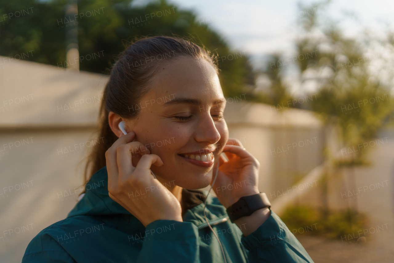 Young woman runner listening music with headphones. Athletic girl listening music while jogging to boost her mood. Outdoor Workout concept.