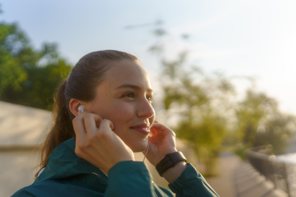 Young woman runner listening music with headphones. Athletic girl listening music while jogging to boost her mood. Outdoor Workout concept.