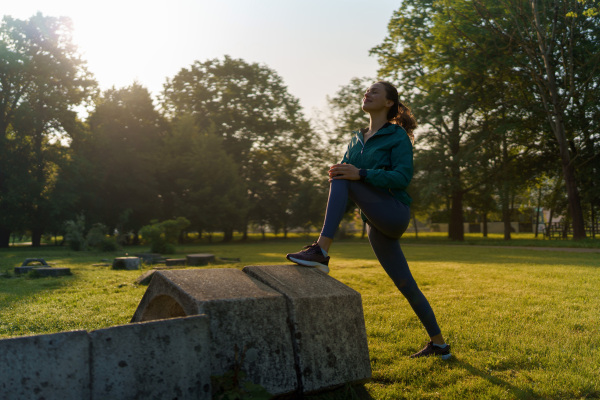 Full lenght portrait of beautiful fitness woman stretching before morning outdoor workout in the city park. Healthy lifestyle concept. Copy space.