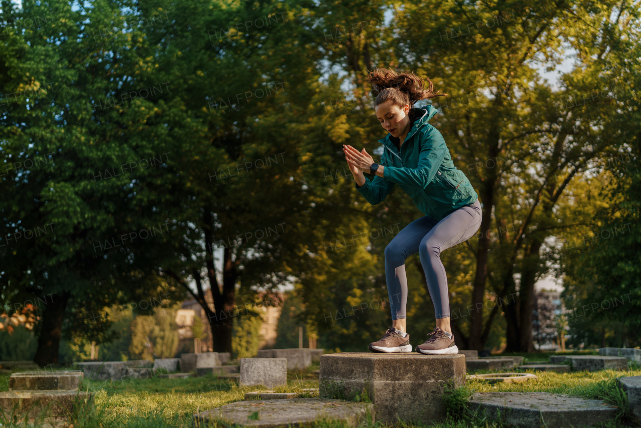 Full lenght portrait of beautiful fitness woman doing squat box jumps in the park. Workout at the park. Outdoor workout concept.