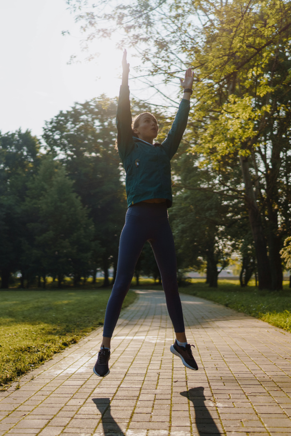 Fitness young woman doing full-body crossfit outdoor workout in the city park. Girl doing jumping jacks, star jumps exercise.