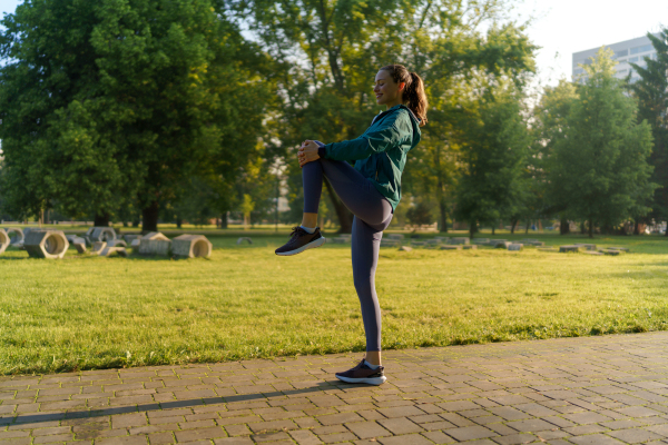 Full lenght portrait of beautiful fitness woman stretching before early morning outdoor workout in the city park. Healthy lifestyle concept. Copy space.