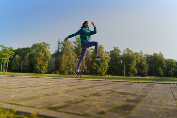 Side view of athletic woman in activewear doing high knees run in the city in the morning. Outdoor workout concept. Banner with copy space.