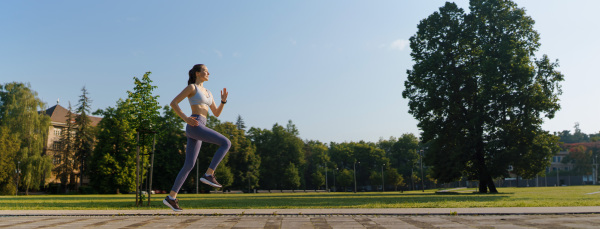 Side view of athletic young woman in activewear running in the city in the morning. Outdoor workout concept.