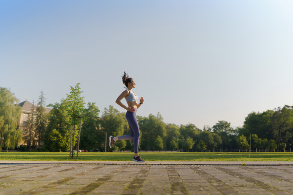 Side view of athletic young woman in activewear running in the city in the morning. Outdoor workout concept. Banner with copy space.