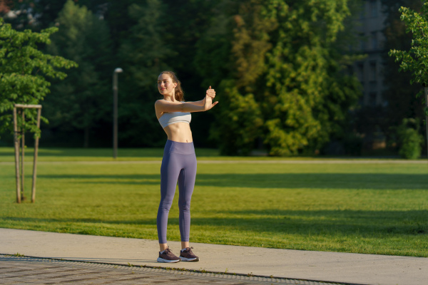 Full lenght portrait of beautiful fitness woman stretching before outdoor workout in the city park. Healthy lifestyle concept. Copy space.