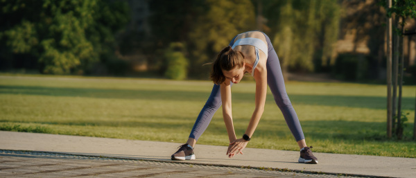 Full lenght portrait of beautiful fitness woman stretching before outdoor workout in the city park. Healthy lifestyle concept. Banner with copy space.