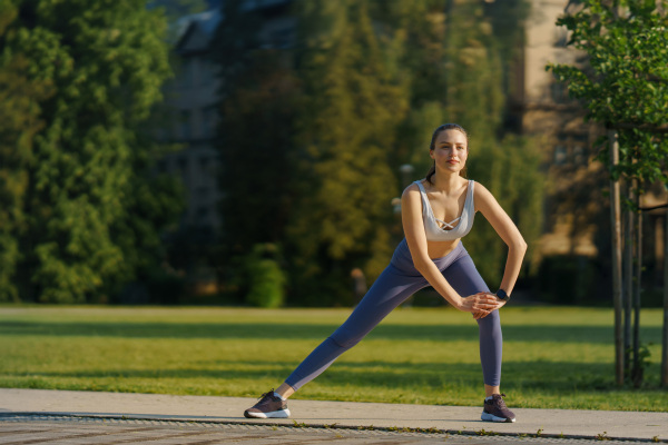 Full lenght portrait of beautiful fitness woman stretching before outdoor workout in the city park. Healthy lifestyle concept. Copy space.