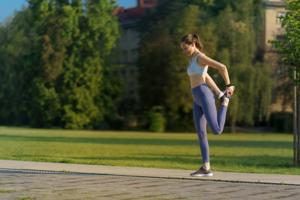 Full lenght portrait of beautiful fitness woman stretching before outdoor workout in the city park. Healthy lifestyle concept. Copy space.