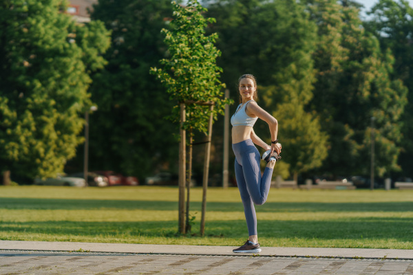 Full lenght portrait of beautiful fitness woman stretching before outdoor workout in the city park. Healthy lifestyle concept. Copy space.