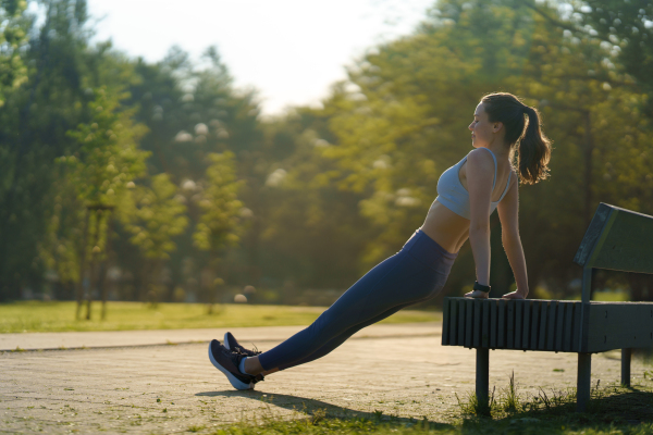 Full lenght portrait of beautiful fitness woman doing reverse push-ups against park bench. Workout at the park. Park bench excercises.