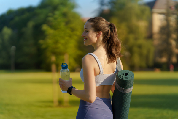 Rear view of beautiful athletic girl in sportswear with yoga mat on shoulder and water bottle heading for a pilates workout.