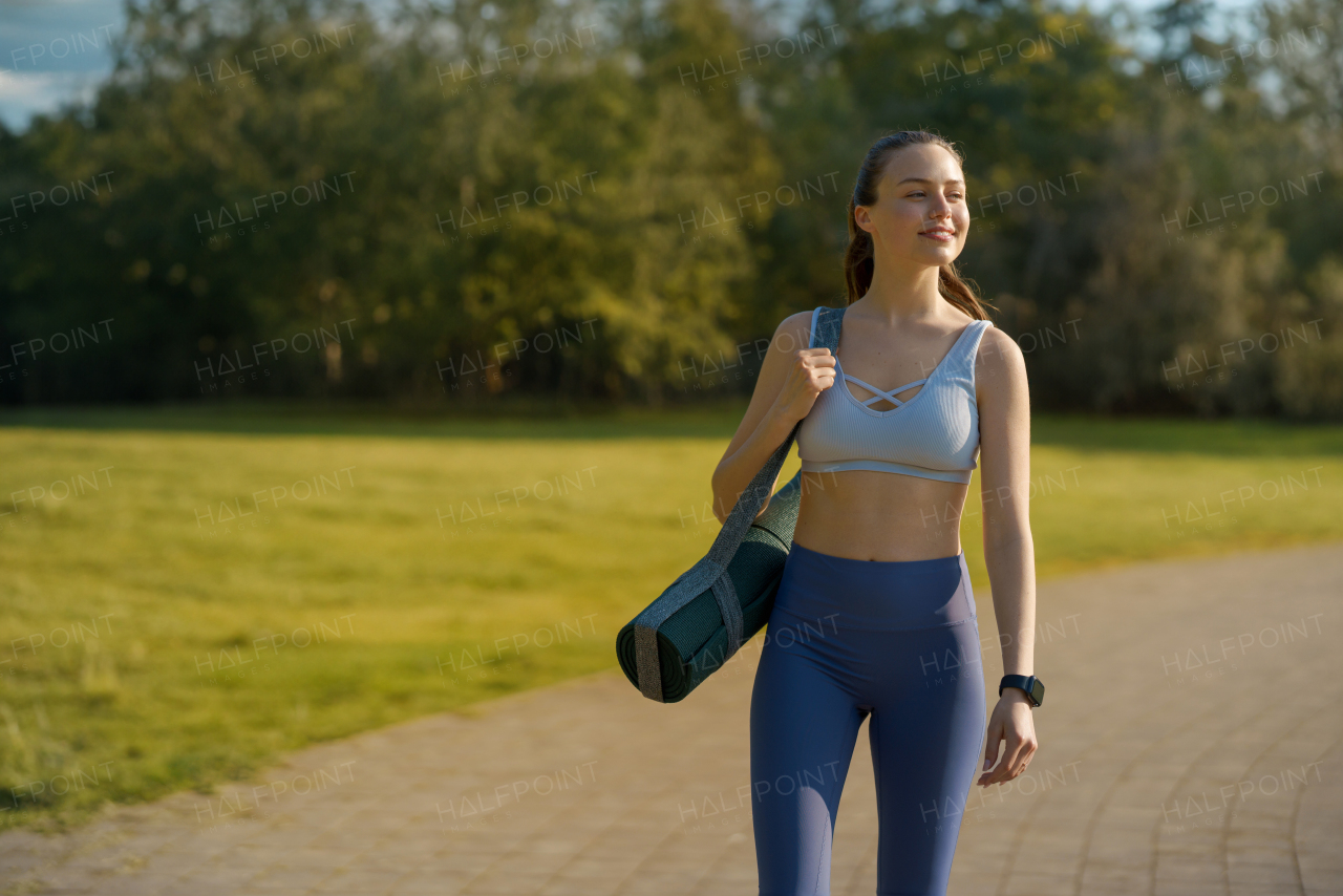 Portrait of beautiful athletic girl in sportswear with yoga mat on shoulder heading for a pilates workout.