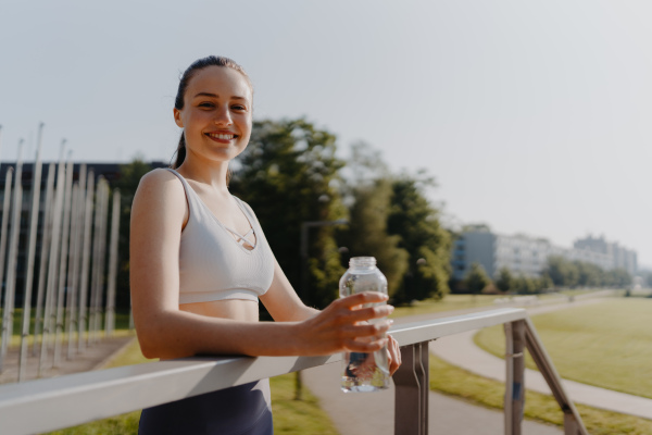 Portrait of sporty woman drinking water from bottle after workout session. Importance of hydration during workout.