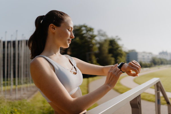 Side view of sporty woman checking her performance on smartwach after workout session. Woman using smartwatch to sending text message, calling.