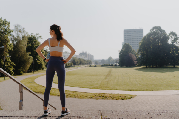 Rear view of young beautiful female runner after jogging up the stairs the city park, enjoying the view. Morning workout in the city. Outdoor workout concept.