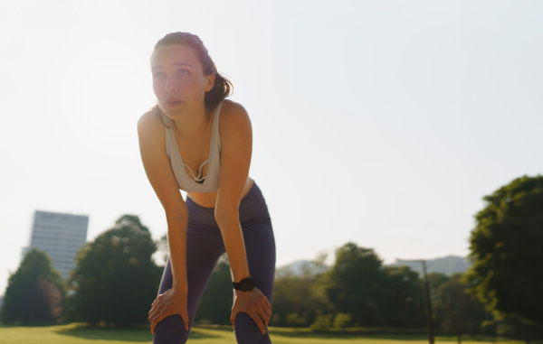 Young woman runner resting after workout session on sunny morning. Doing deep breathing excercises.