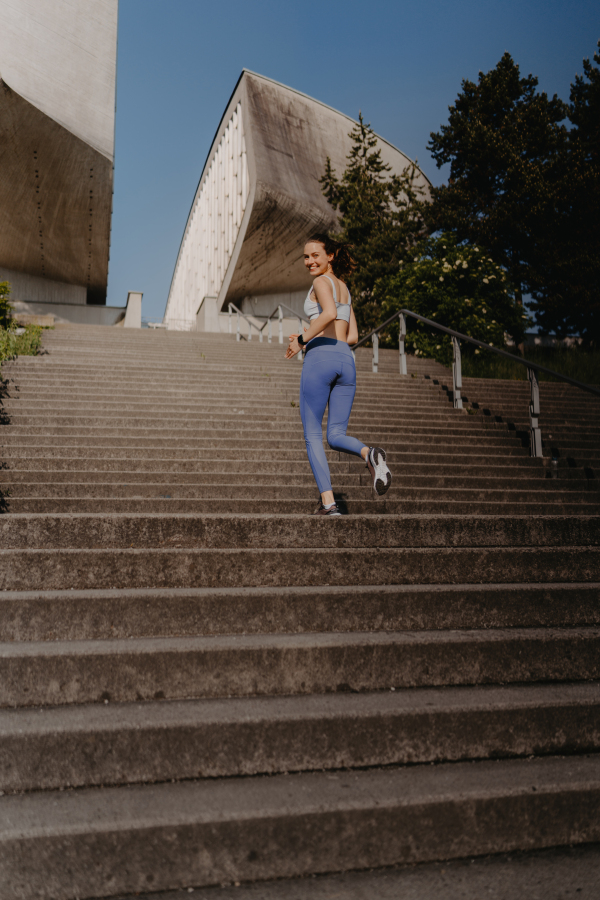 Portrait of sporty woman running on the concrete stairs in city park. Female athlete in sportswear doing stair workout outside. Healty lifestyle concept.