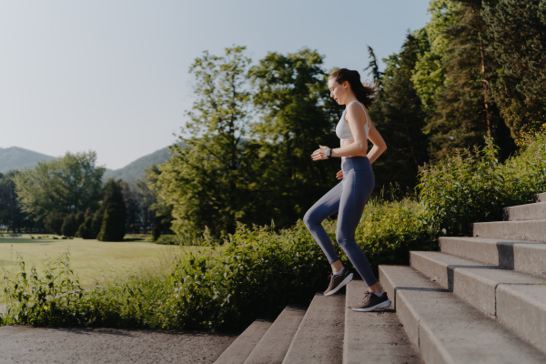 Sporty woman running down the concrete stairs in city park. Female athlete in sportswear doing stair workout outside. Healty lifestyle concept.