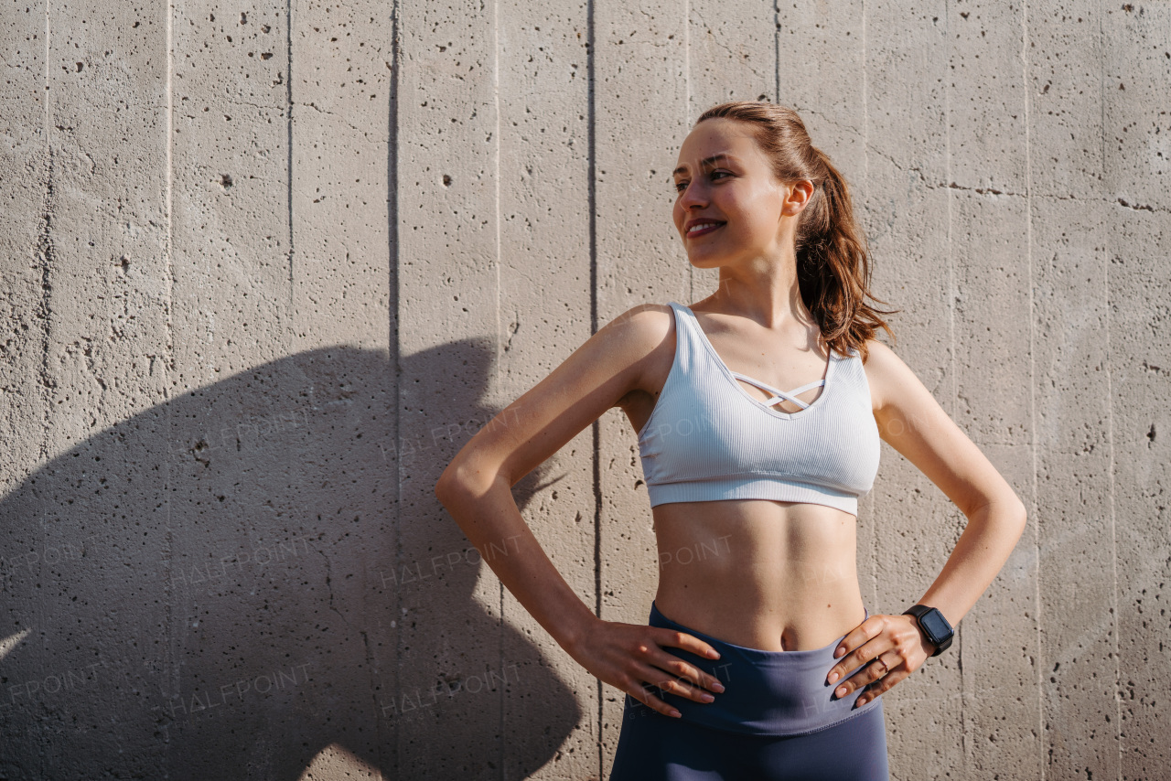 Portrait of young sporty woman in sportswear excercising outdoors. Fitness woman in front of concrete wall in the city. Healthy lifestyle concept. Street workout.