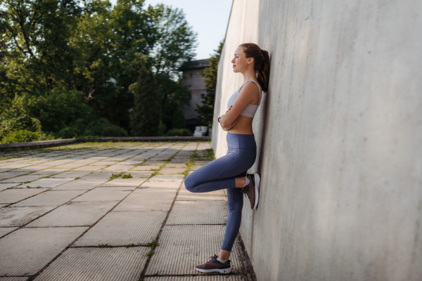 Side view of young sporty woman in sportswear excercising outdoors. Fitness woman in front of concrete wall in the city. Healthy lifestyle concept. Street workout.