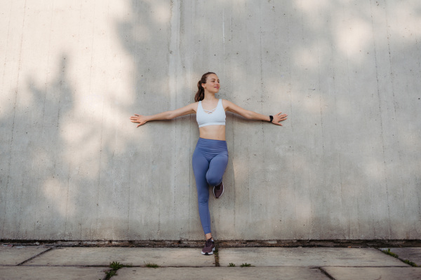 Portrait of young sporty woman in sportswear excercising outdoors. Fitness woman in front of concrete wall in the city. Healthy lifestyle concept. Street workout.