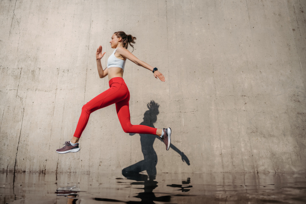 Female athlete in sportswear exercising in the city. Running in front of concrete wall casting shadow. Banner with copy space.