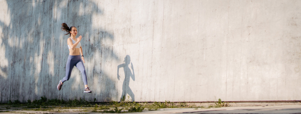 Female athlete in sportswear exercising in the city. Running in front of concrete wall casting shadow. Banner with copy space.