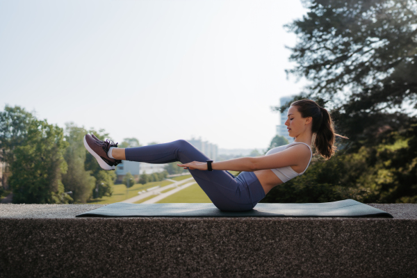 Side view of young sporty woman doing elevated crunches on gym mat. Fitness woman doing abs exercises outdoors. Healty lifestyle concept, street workout.