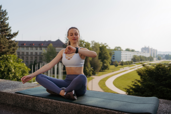 Sporty woman checking her performance on smartwach after workout session. Woman using smartwatch to sending text message, calling. Cross-legged sitting.